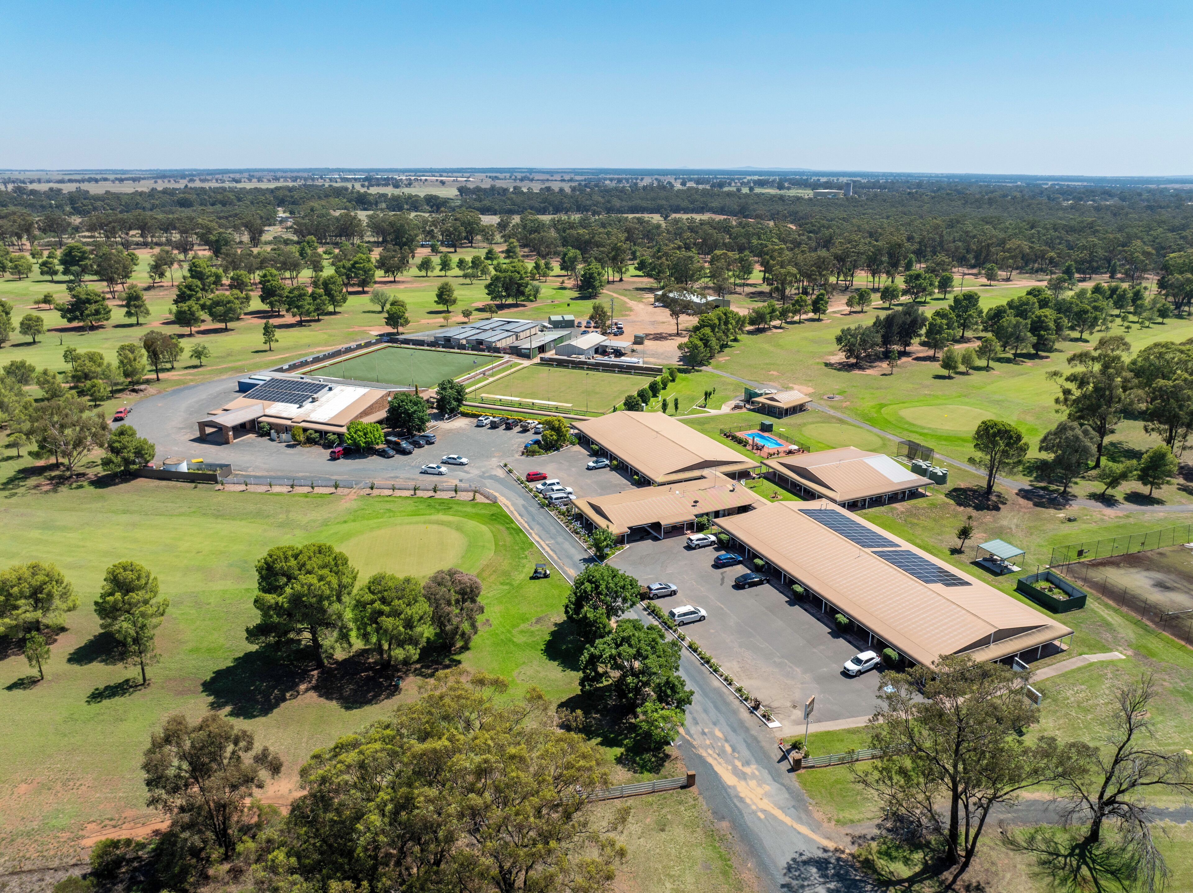 An aerial view of a golf course with multiple buildings, parking areas, and surrounding greenery.