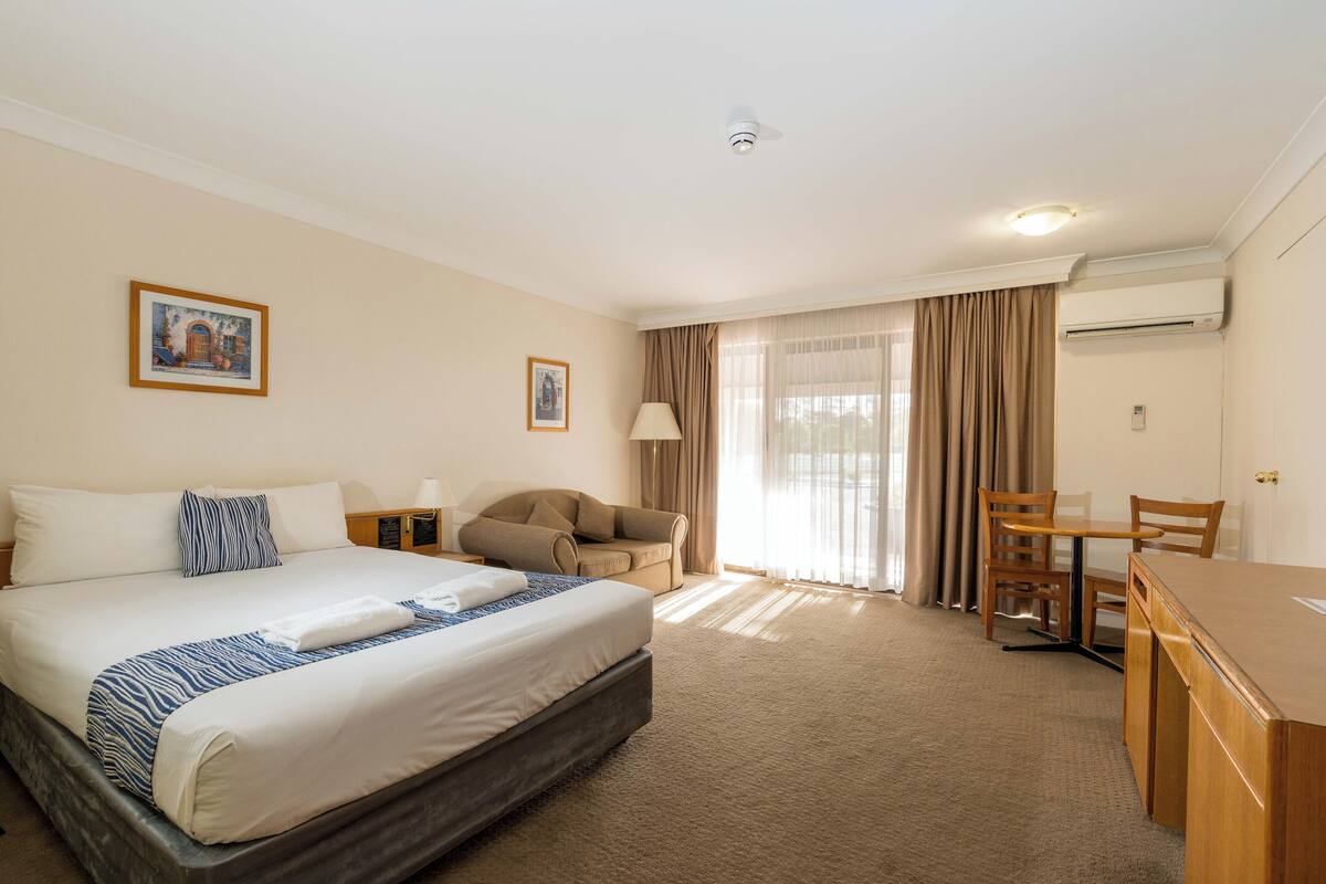 A hotel room with a bed, a desk, a chair, a sofa, and a window with curtains.