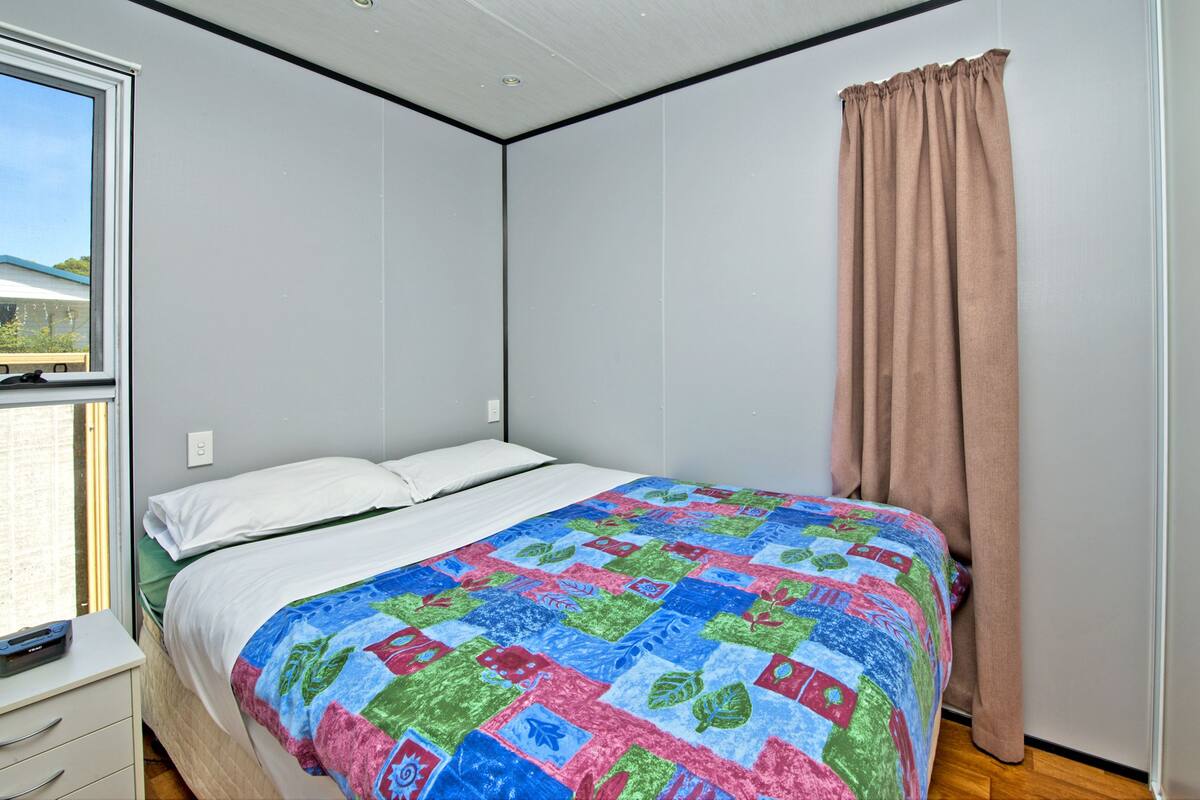 A bedroom with a bed, white walls, a window, and a curtain.