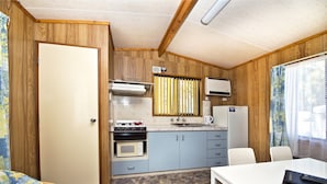 Cocina compacta con estufa, microondas y refrigerador, paredes de madera y un comedor con mesa y sillas.