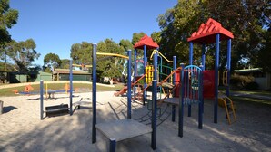 Un parque infantil con diversas estructuras de juego, incluyendo toboganes y juegos de escalada, rodeado de arena y árboles.
