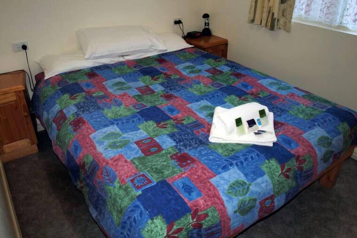 A neatly made bed with a colorful quilt, a white pillow, and a white towel on the bed.