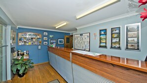 Una zona de recepción con mostrador de madera, cuadros en la pared, un tablón de anuncios y una planta en maceta.