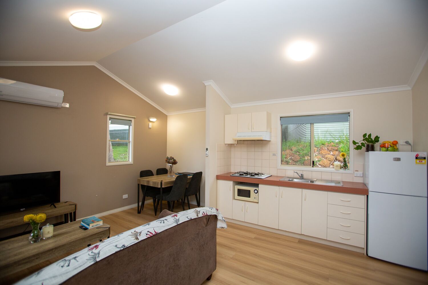 A compact kitchen with a dining area, a flat-screen TV, and a sofa.
