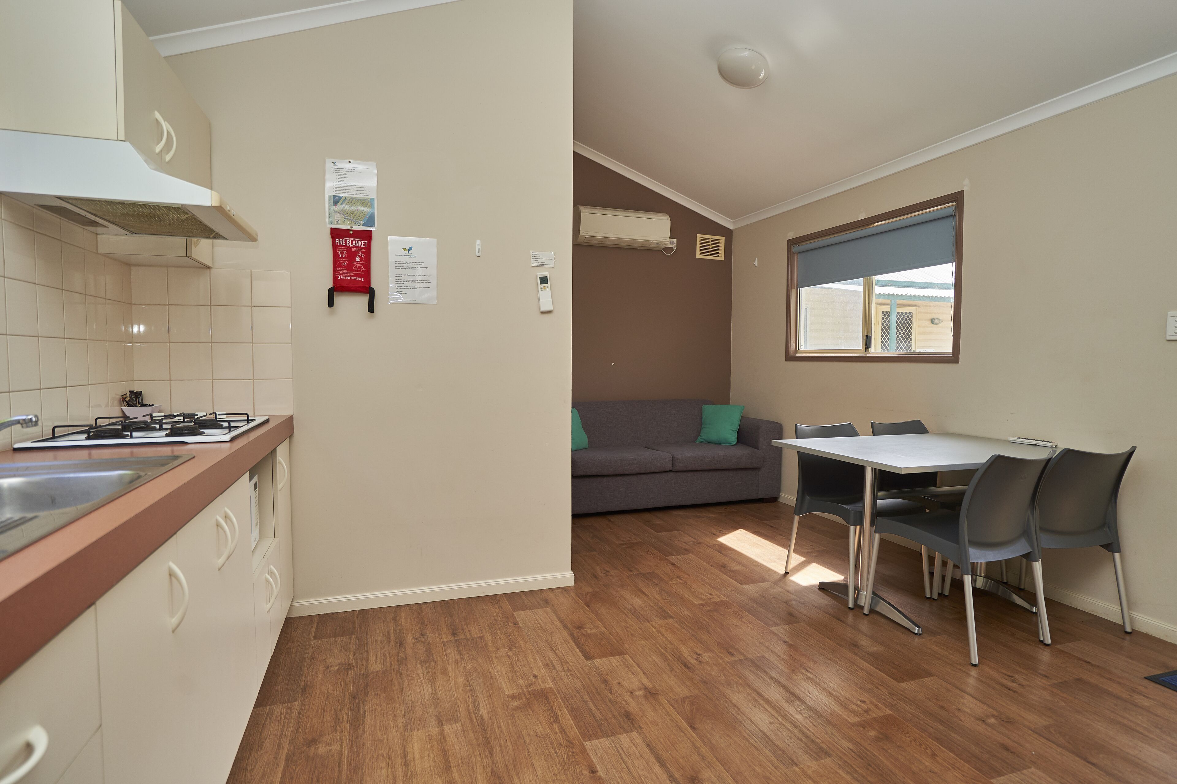 A compact kitchen with a gas stove, a sink, and a window. There is a dining area with a table and chairs.