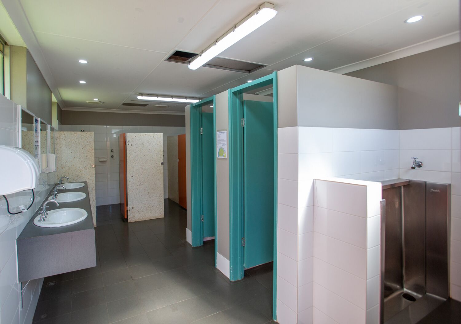 Eine öffentliche Toilette mit drei Waschbecken, einem Spiegel und einer Toilette.