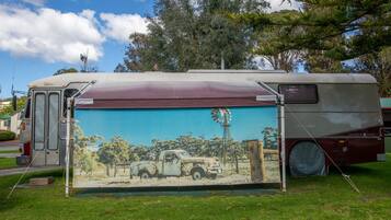 A vintage camper van parked on a grassy area with a mural of a rural scene on its side.