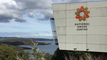 A sign for the National Anzac Centre with a scenic view of hills and a lake in the background.