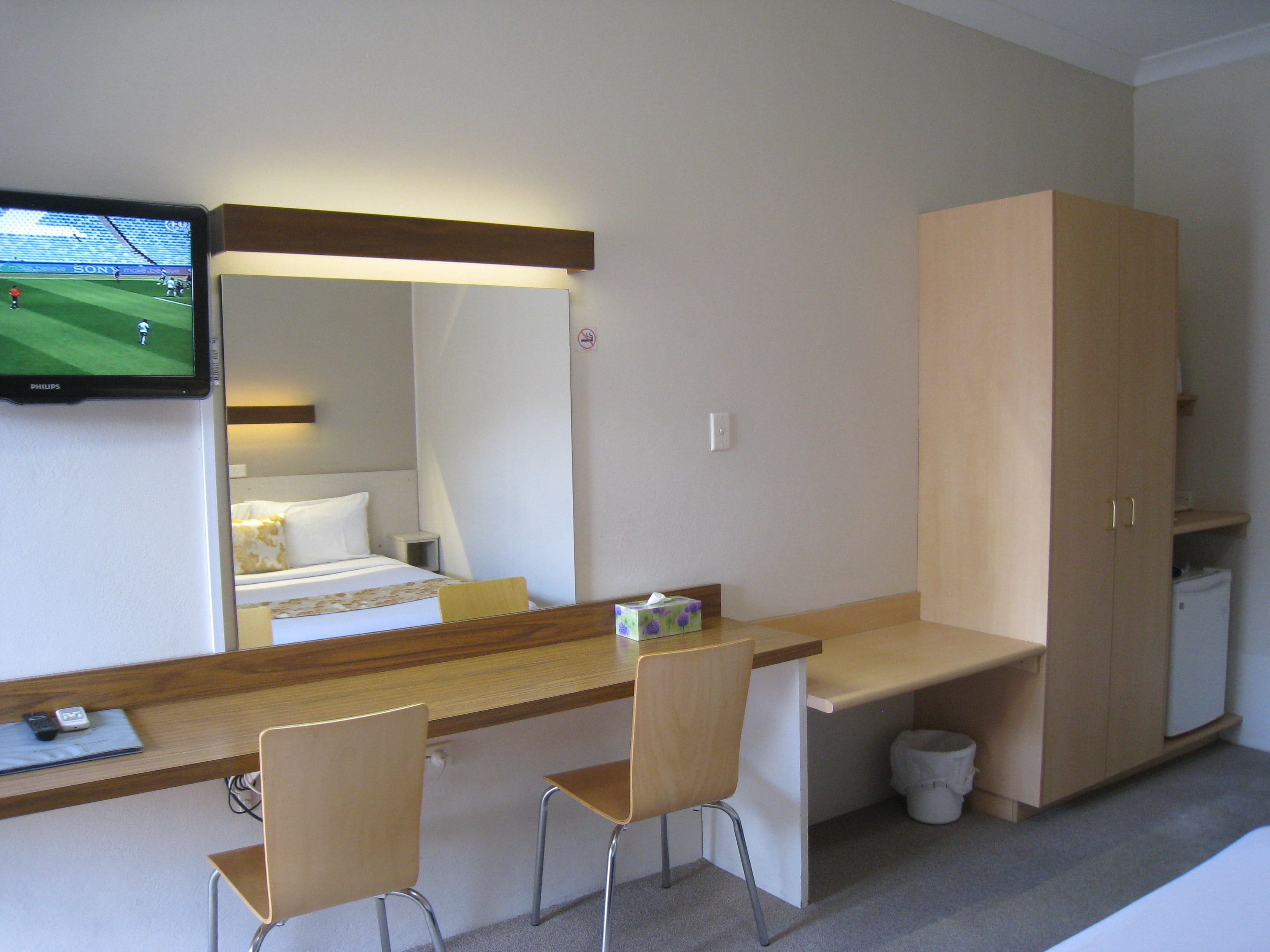 A hotel room with a bed, a desk with two chairs, a television, and a wardrobe.