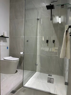 A modern bathroom with a glass-enclosed shower, a toilet, and a towel rack.