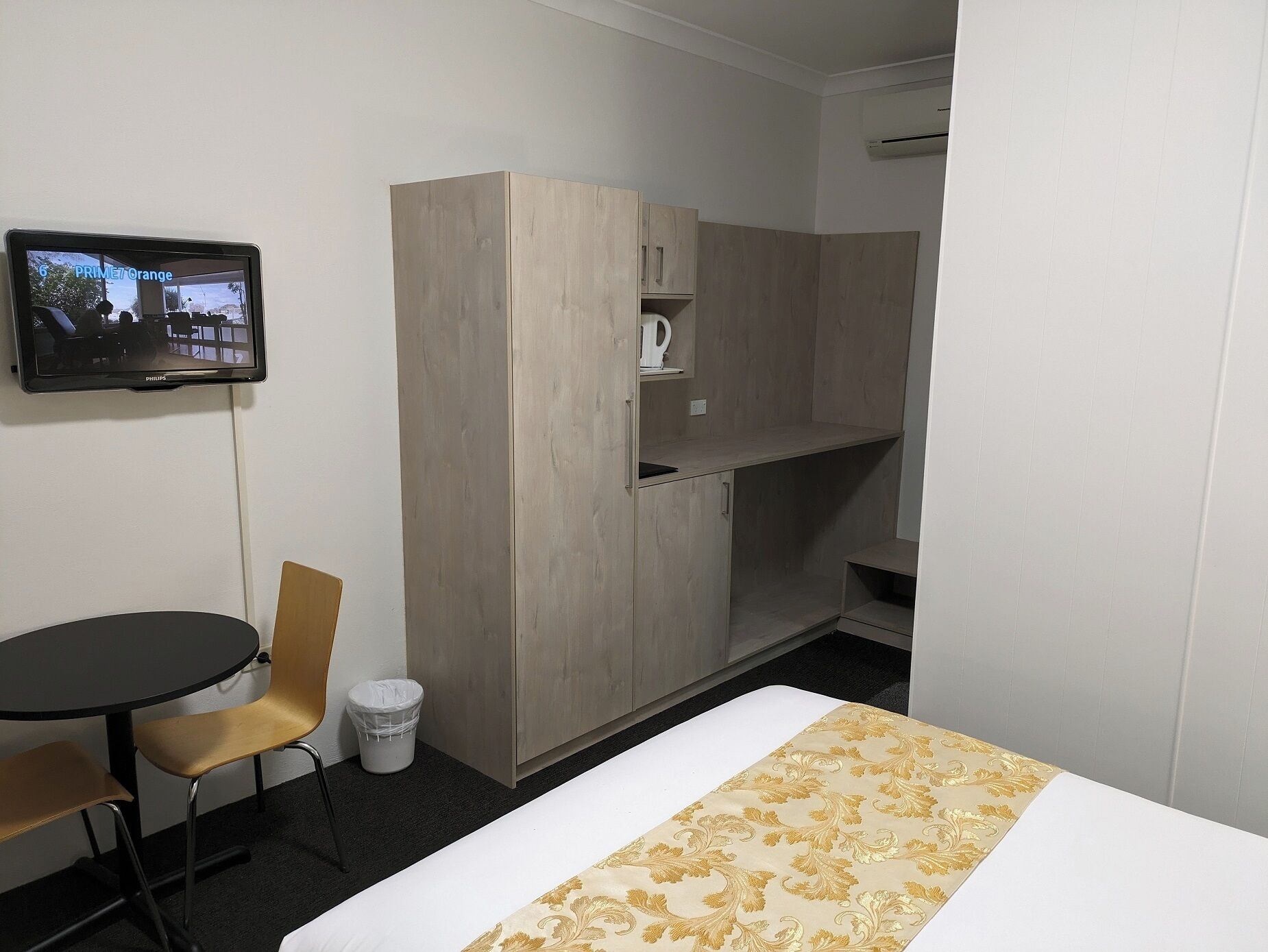 Una habitación de hotel con cama, escritorio, silla, armario y televisión en la pared.