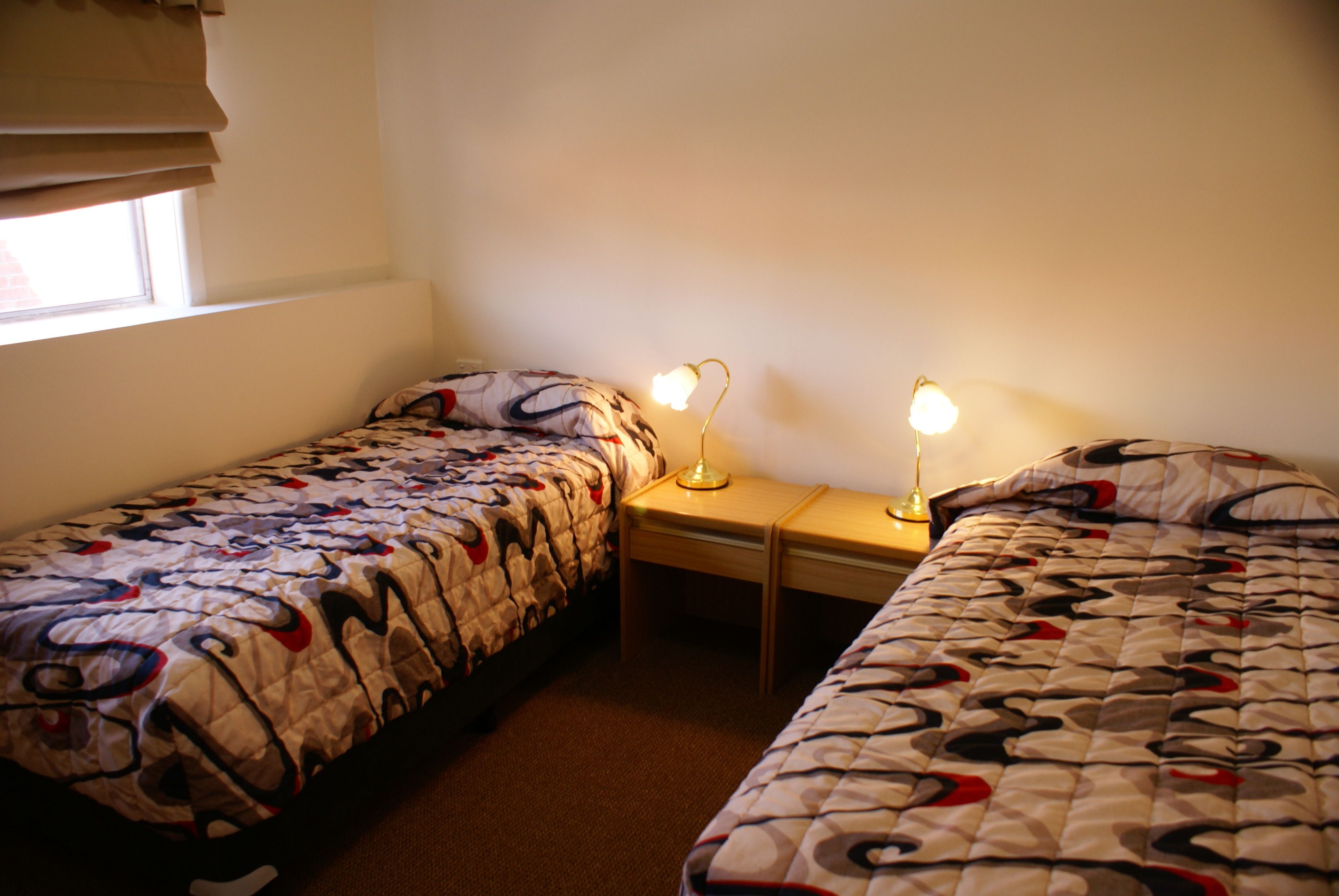 A bedroom with two single beds, a nightstand, and a lamp between them.