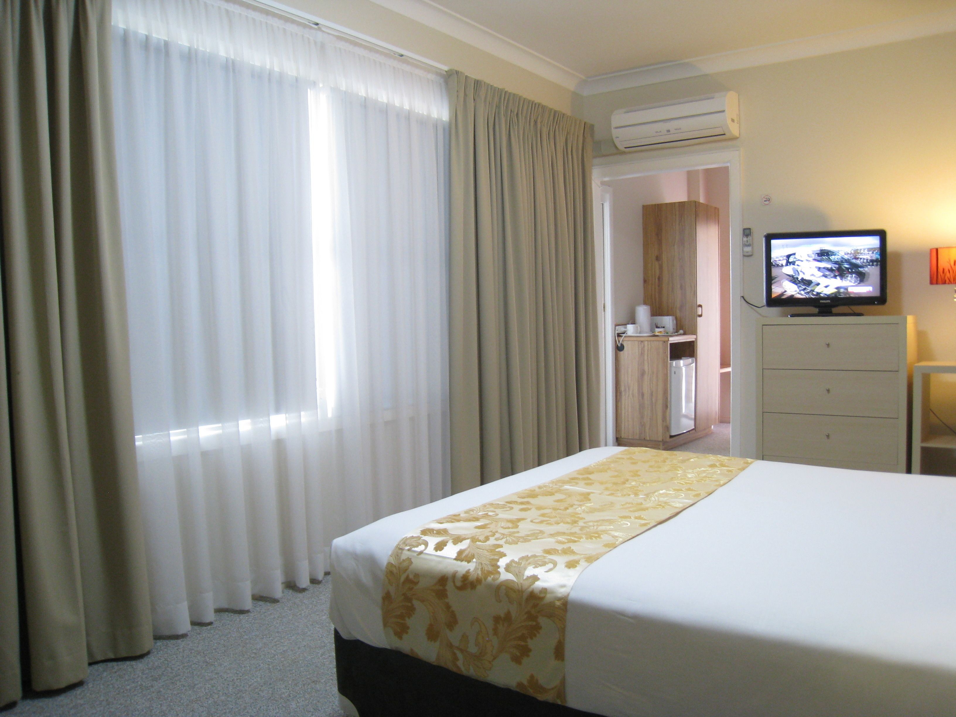 Hotelkamer met een bed, gordijnen, een airconditioner, een televisie en een klein kastje.
