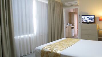 Hotelkamer met een bed, gordijnen, een airconditioner, een televisie en een klein kastje.