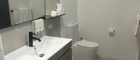 Ein modernes Badezimmer mit einem weißen Waschbecken, einem dunklen Holz-Waschtisch, einem Spiegel, einer Toilette und einer Duschkabine.