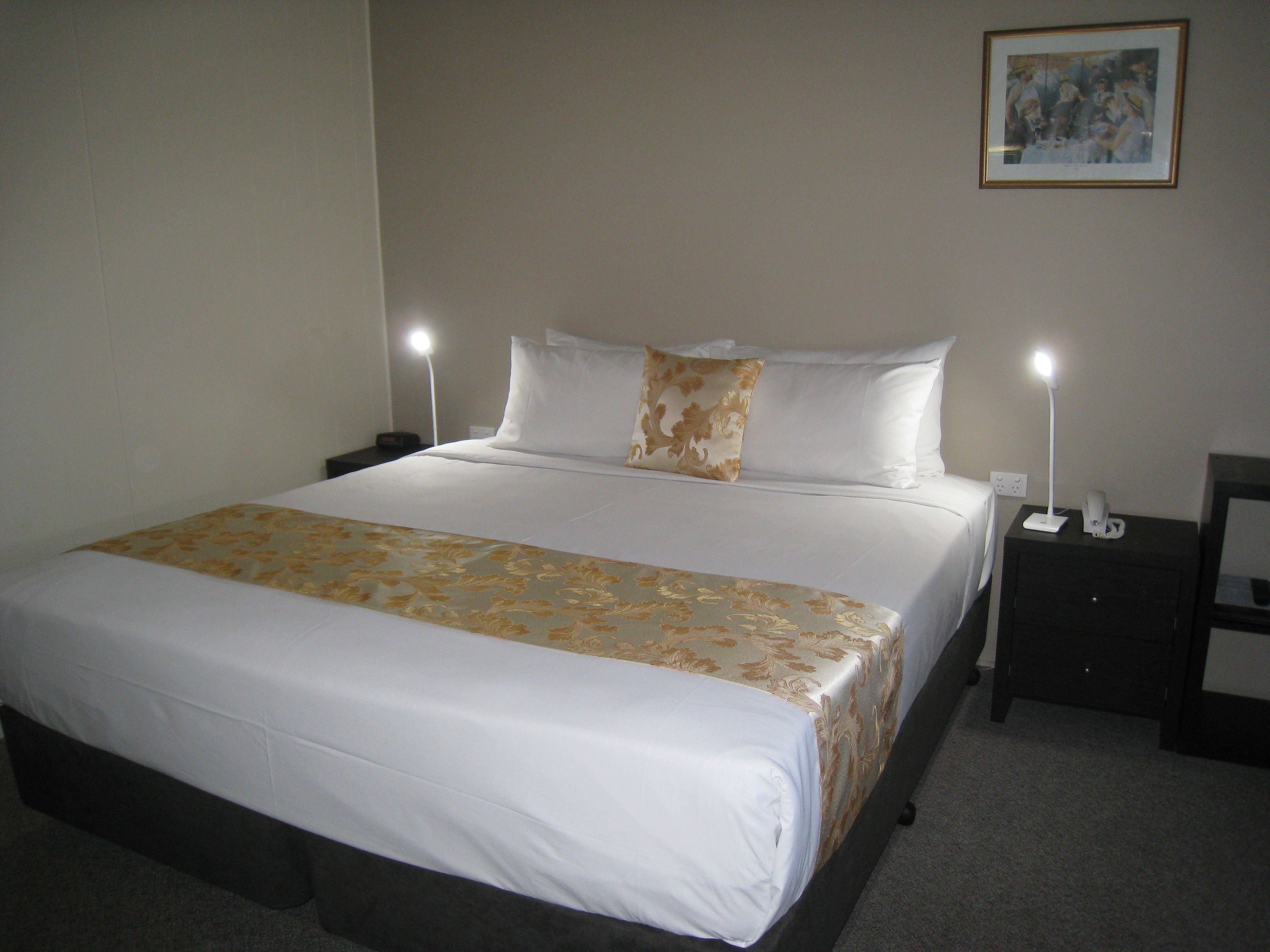 A neatly made bed with a floral bedspread, two bedside lamps, and a framed picture on the wall.