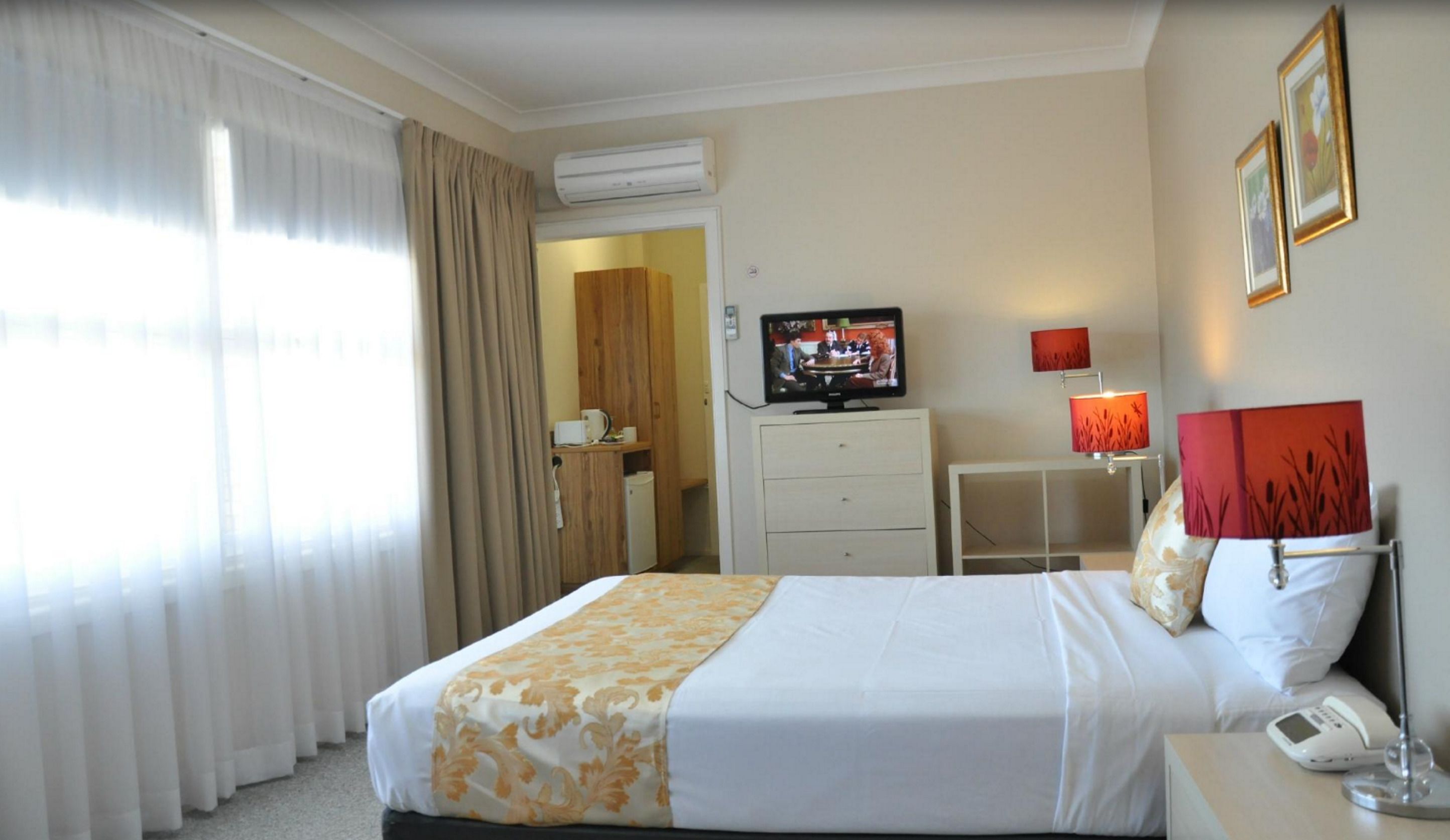 A hotel room with a bed, a television, a desk, a lamp, and a phone.