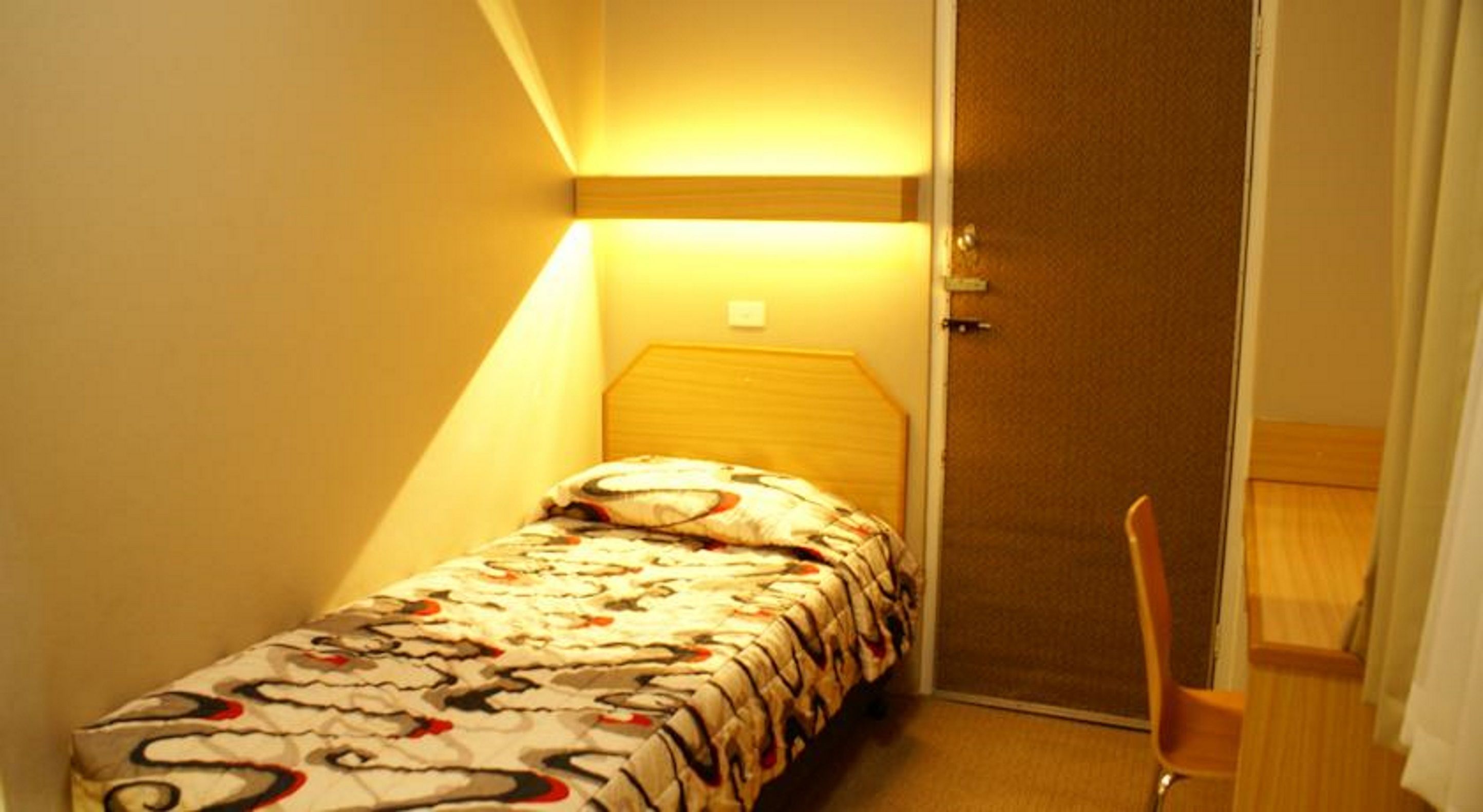 Una habitación pequeña con cama individual, techo inclinado y lámpara de noche.