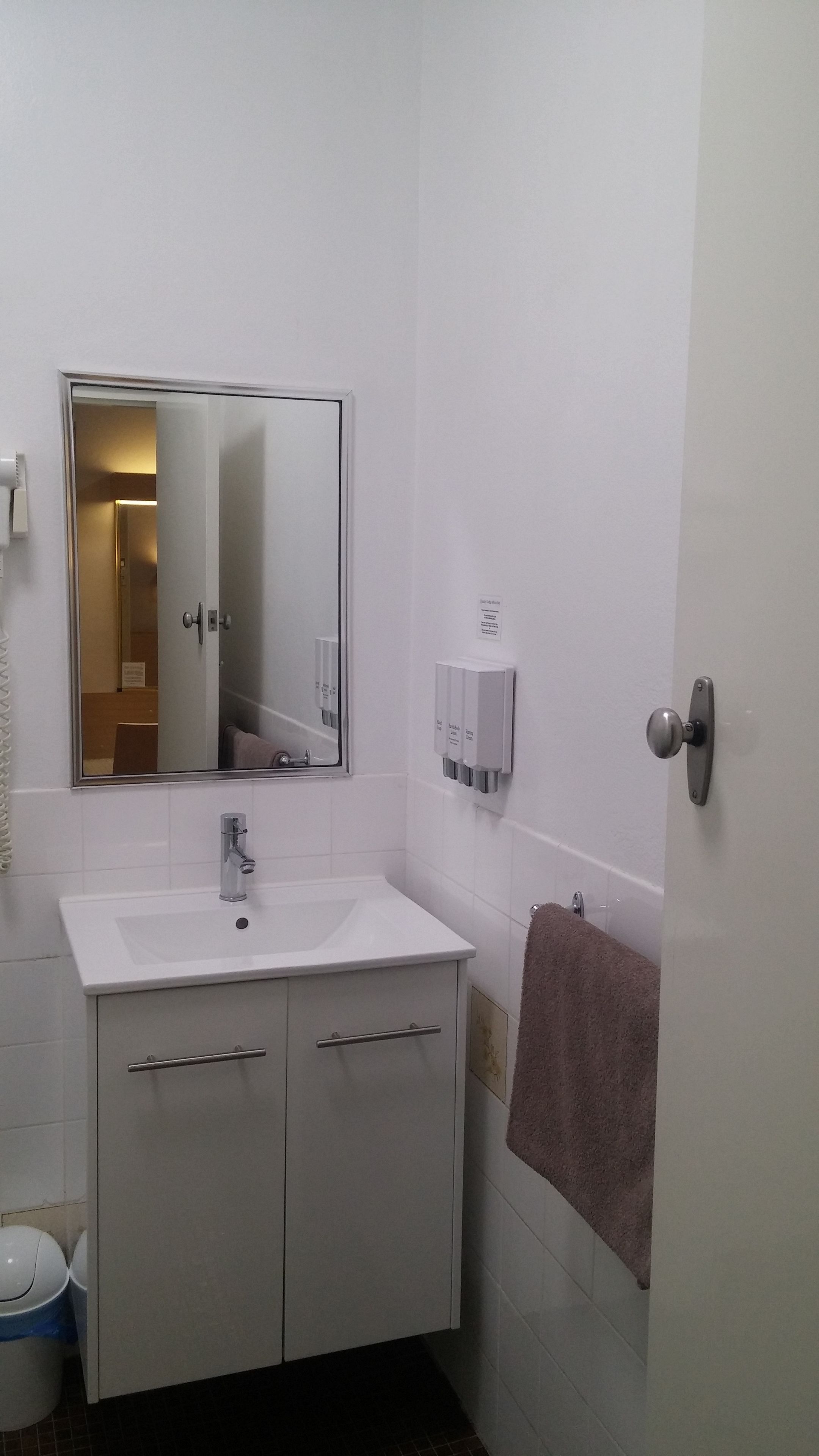 A bathroom with a white sink, a mirror, a towel rack, and a door.