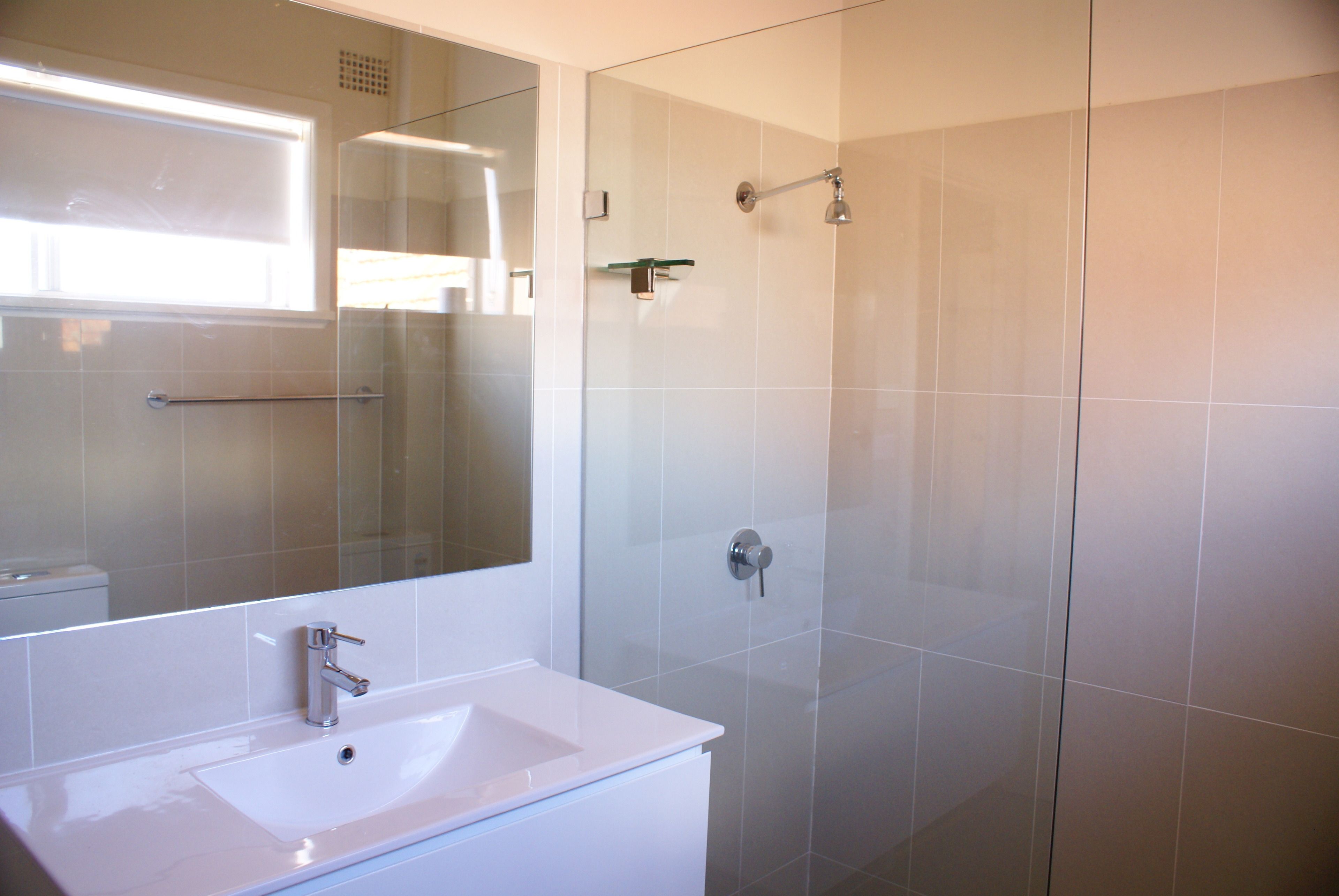 Un baño con lavamanos blanco, cabina de ducha de vidrio y un espejo grande.