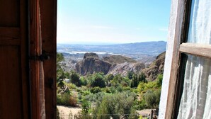 Vista desde una ventana con marco de madera, sobre un valle con vegetación y terreno rocoso.