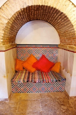 Um recanto acolhedor com um banco estampado, um arco decorativo e uma parede revestida de azulejos.