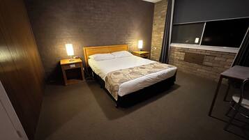 A hotel room with a single bed, two bedside tables with lamps, a window with curtains, and a small stool.