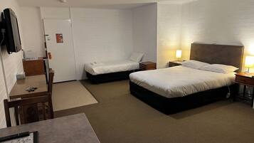 Ein Hotelzimmer mit zwei Einzelbetten, einem Schreibtisch mit Stuhl, einem kleinen Tisch und einem an der Wand befestigten Fernseher.