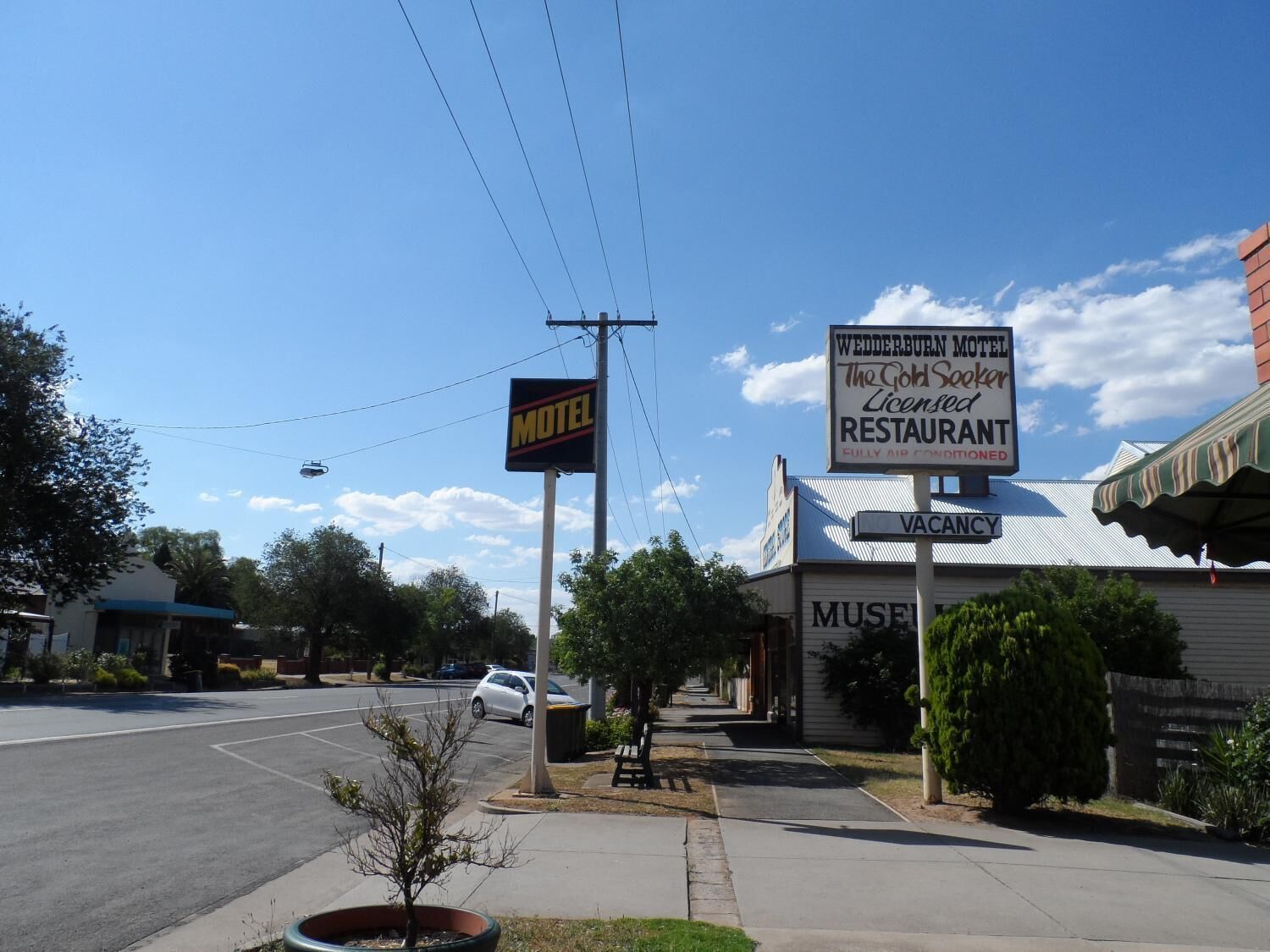 A motel with a signboard, a parking lot, and a building with a 'VACANCY' sign.