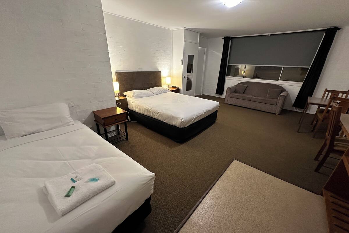 A hotel room with two beds, a sofa, a dining table, and a window with curtains.