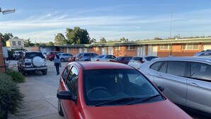 Un parcheggio con diverse auto, tra cui un SUV rosso e una berlina argento. Si vede un edificio sullo sfondo con un cartello che riporta la scritta 'STEGESBURG HOTEL'.