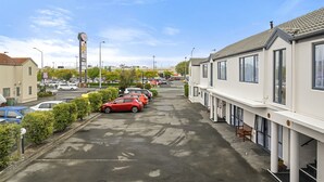 A street view with parked cars, a row of white buildings with large windows, and a clear sky. - Riccarton Mall Motel (Christchurch)