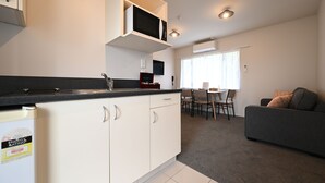 A compact kitchen with white cabinets, a microwave, and a dining area with a table and chairs. - Riccarton Mall Motel (Christchurch)