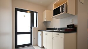 A compact kitchen with white cabinets, a black countertop, a microwave, and a small refrigerator. - Riccarton Mall Motel (Christchurch)