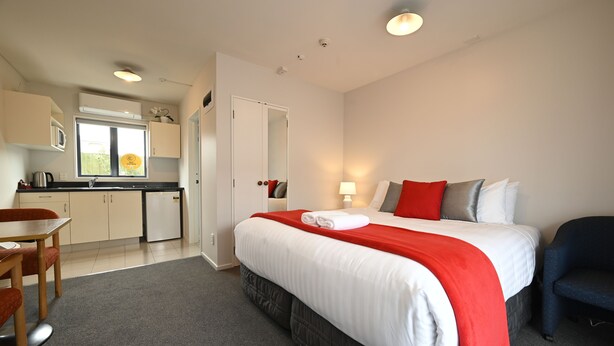 A hotel room with a bed, a desk, a chair, a kitchenette, and a bathroom. - Riccarton Mall Motel (Christchurch)