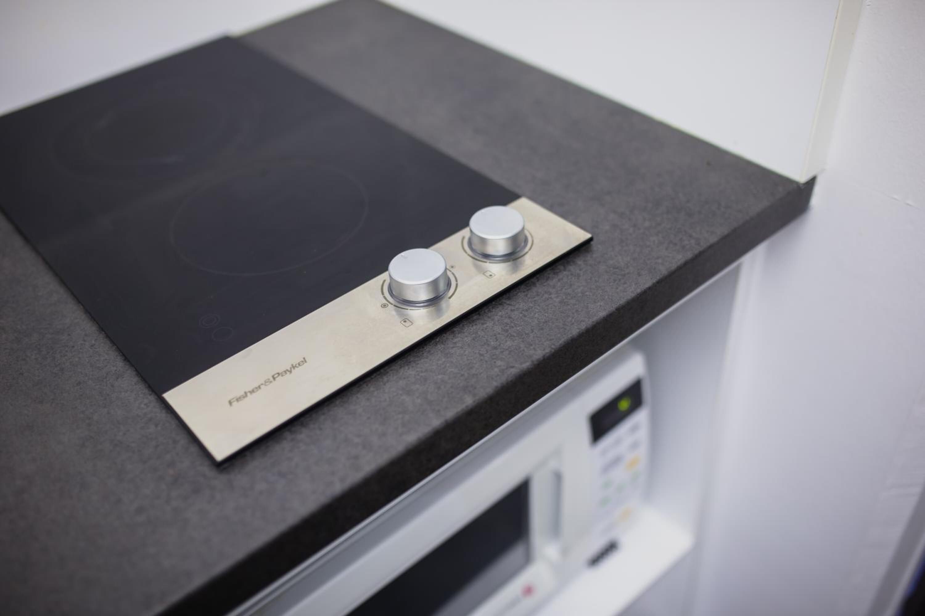 A kitchen with a black countertop, a stainless steel induction cooktop, and a microwave.