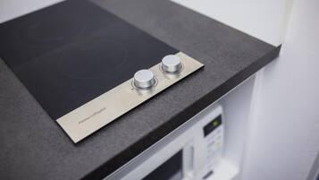 A kitchen with a black countertop, a stainless steel induction cooktop, and a microwave.