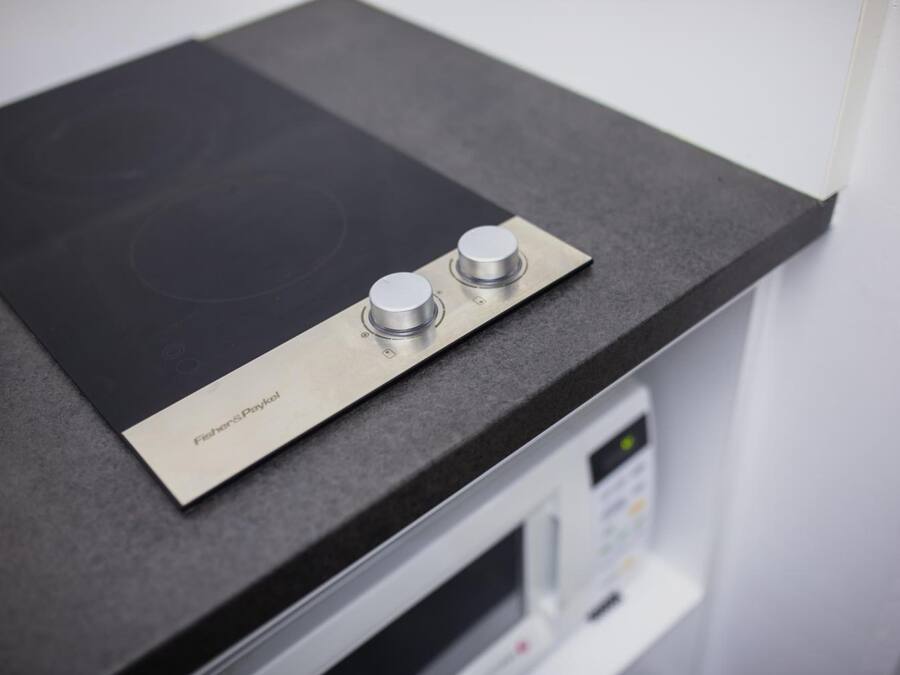 A kitchen with a black countertop, a stainless steel induction cooktop, and a microwave.