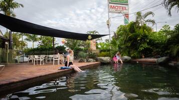 A swimming pool area with a shaded patio, palm trees, and a motel sign.