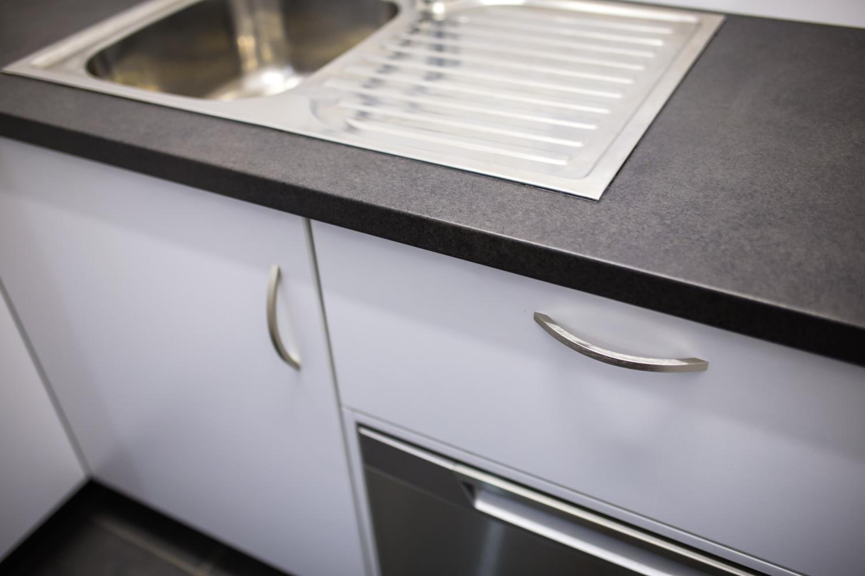 A kitchen with a stainless steel sink, a black countertop, and white cabinets with silver handles.