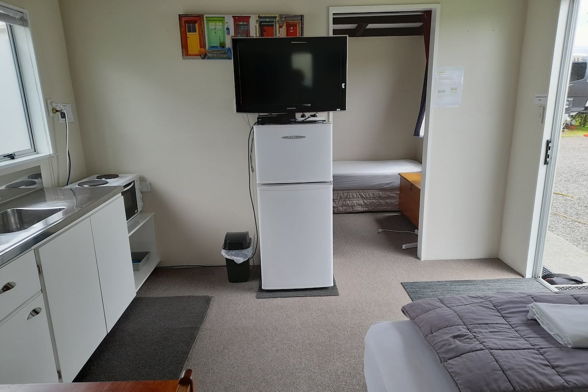 A compact room with a kitchenette, a bed, and a TV.