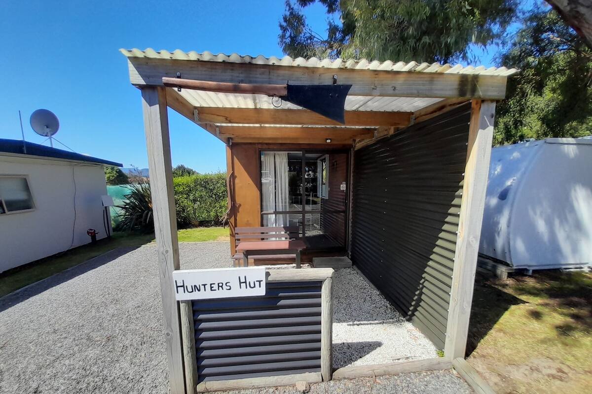 A small, rustic building with a wooden bench and a sign reading "Hunters Hut."
