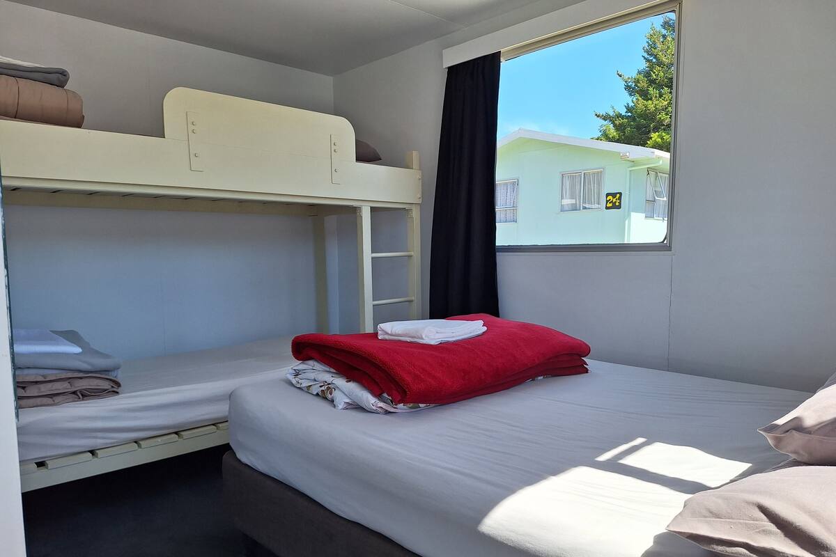 A bunk bed room with a window, a ladder, and a view of a building outside.
