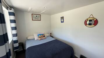 Una cama bien hecha con una manta azul, una cortina a rayas y un adorno de boia en la pared.