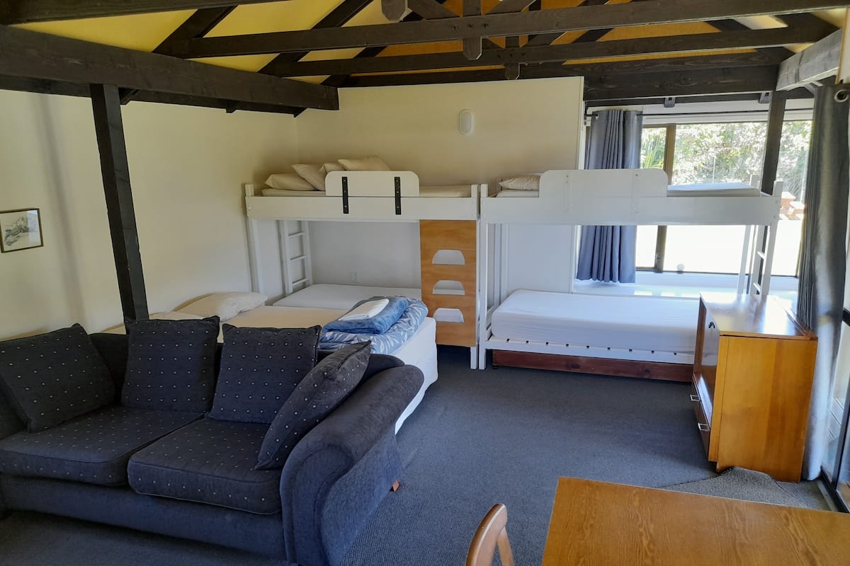 A compact room with bunk beds, a sofa, a wooden table, and a chair.