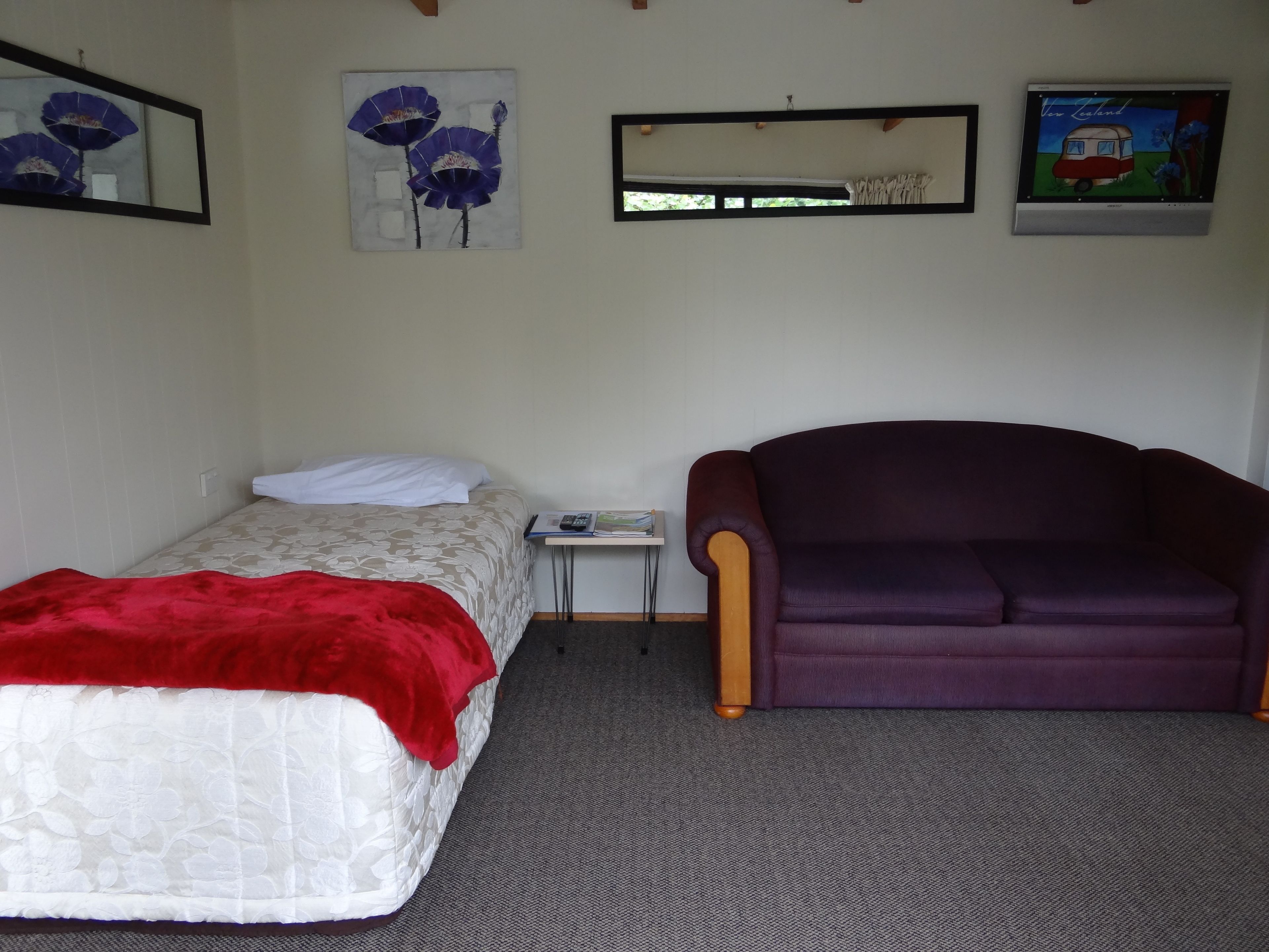 A small, neatly arranged room with a bed, a purple armchair, and a small table.