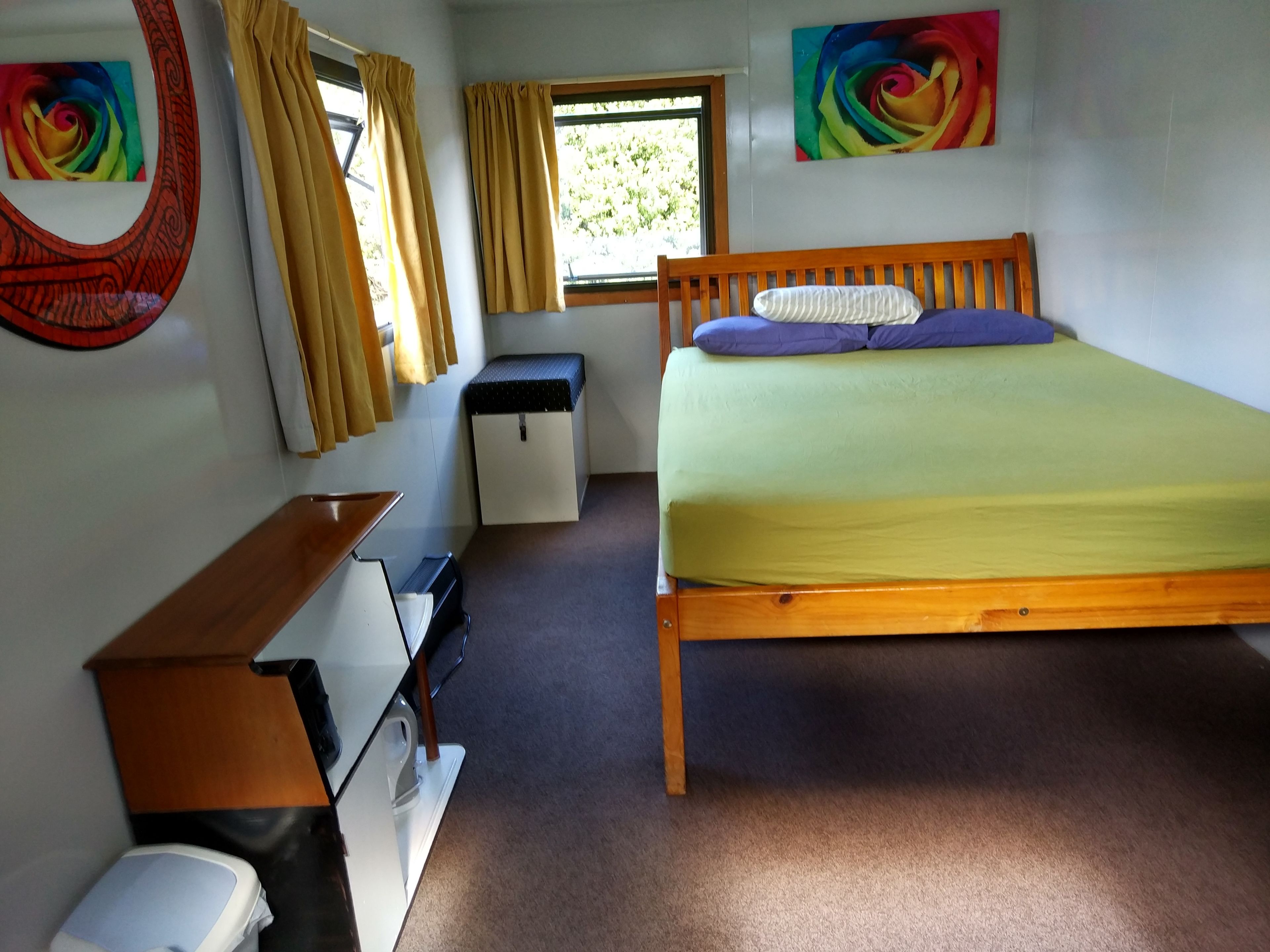 A small, neatly arranged bedroom with a single bed, a desk, a chair, a small wardrobe, and a window with curtains.