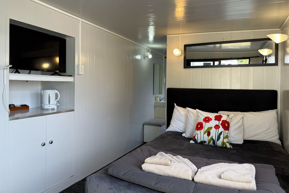 A neatly arranged hotel room with a bed, a coffee maker, a TV, and a small bathroom area.