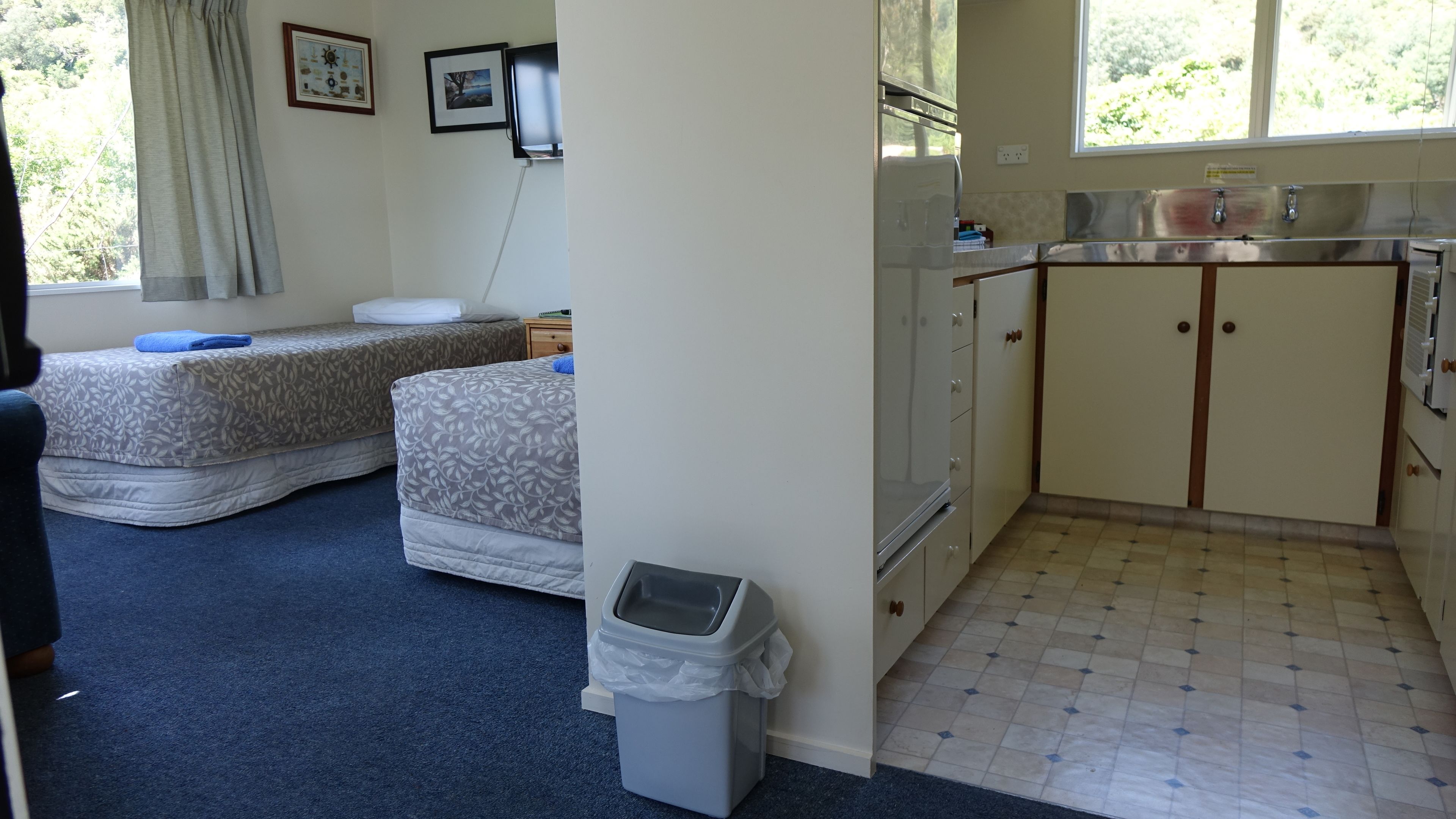 Une chambre de taille réduite comprenant deux lits, une petite kitchenette et une salle de bain.