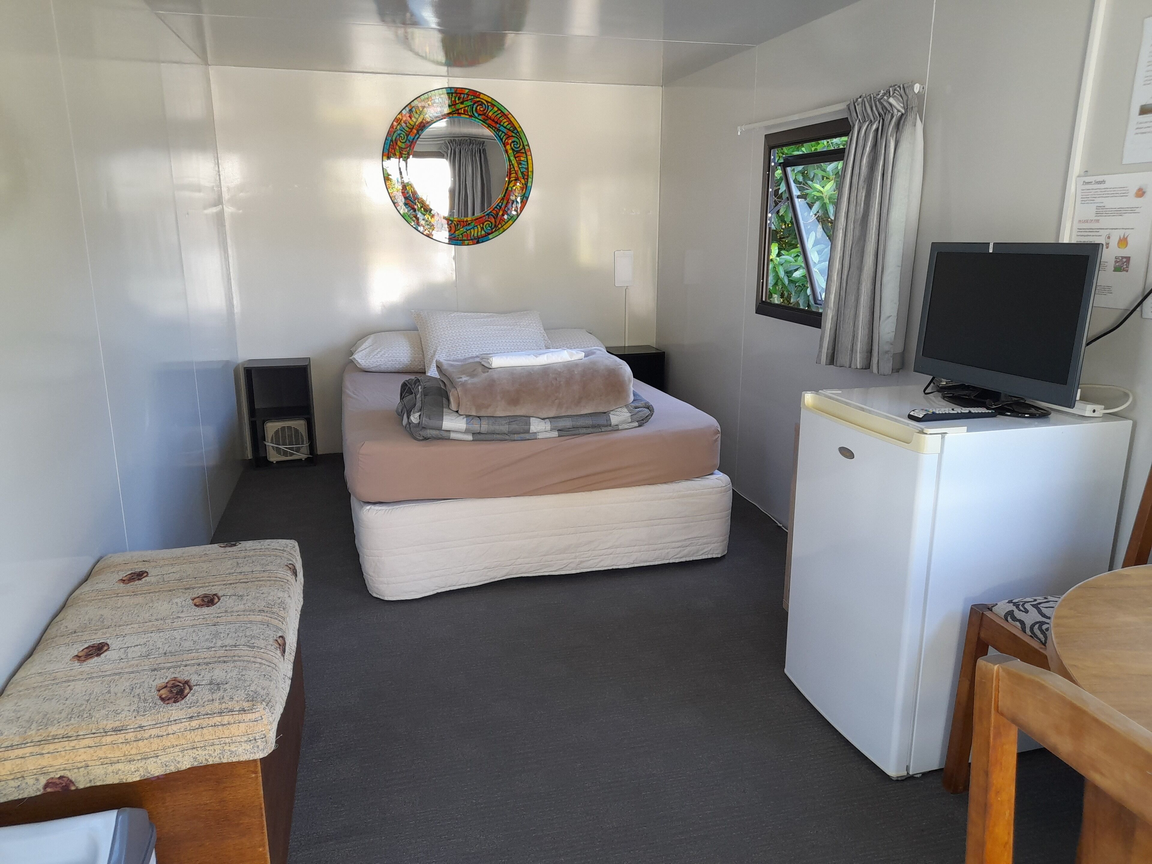 A compact room with a bed, a small desk, a television, and a window with curtains.